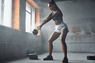 Full length of beautiful young African woman exercising with kettlebell in gym