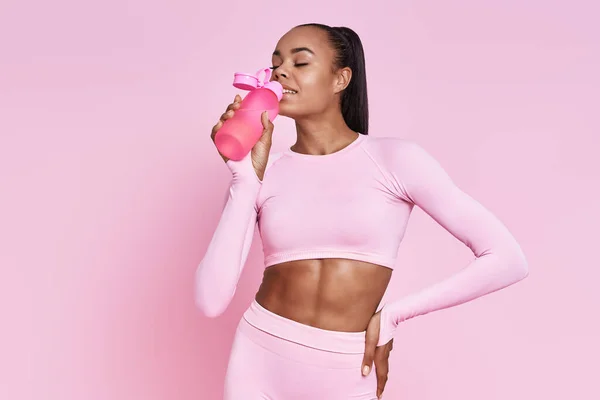 Happy African Woman Sports Clothing Drinking Water Pink Background —  Fotos de Stock