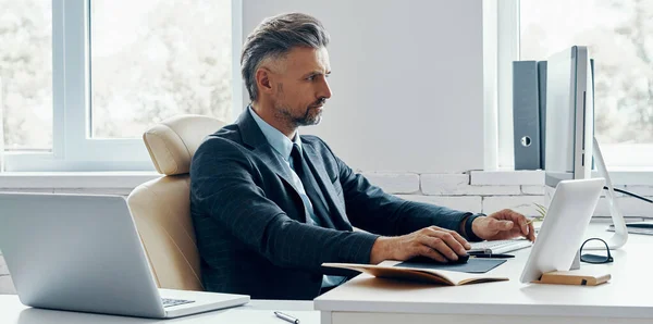 Handsome mature man in formal business wear using computer while sitting at his working place