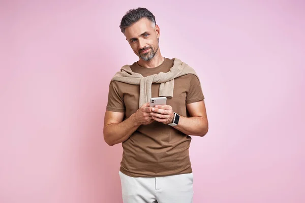Fashionable Mature Man Holding Smart Phone While Standing Pink Background — ストック写真
