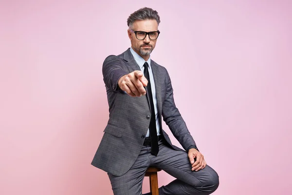 Confident Mature Man Formalwear Pointing Camera While Sitting Pink Background — Foto Stock