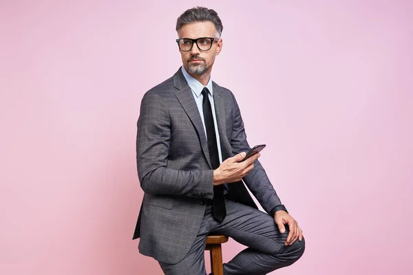 Handsome Mature Man Formalwear Holding Smart Phone While Sitting Pink — Stock fotografie