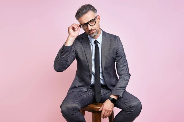 Handsome Mature Man Formalwear Adjusting Eyeglasses While Sitting Pink Background — Fotografia de Stock