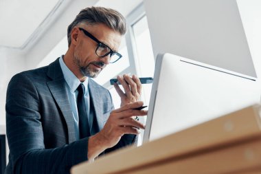 Concentrated businessman using loud speaker on phone while pointing computer monitor in the office