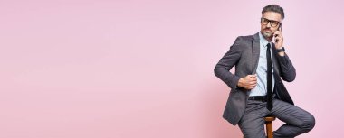 Handsome mature man in formalwear talking on mobile phone against pink background