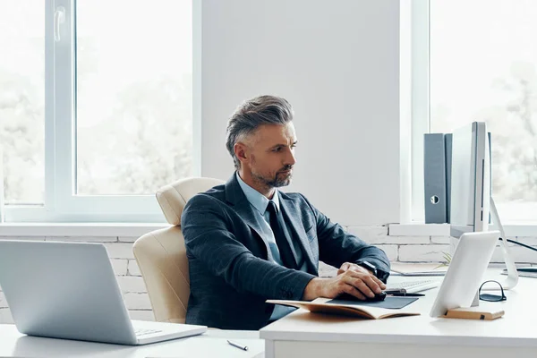 Confident mature man in formal business wear using computer while sitting at his working place