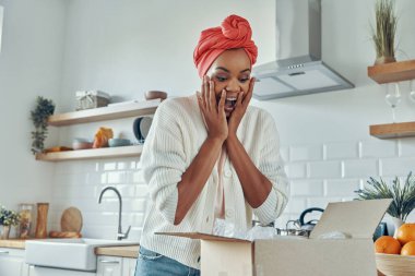Şaşırmış Afrikalı bir kadın mutfakta dururken kutunun kapağını açıp yüzüne dokunuyor.