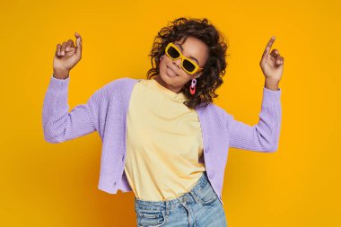 Sarı arka planda dans eden gözlüklü güzel Afrikalı kadın.