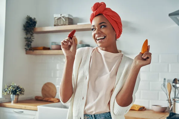 Mulher Africana Bonita Segurando Pimentas Sorrindo Enquanto Estava Cozinha Doméstica — Fotografia de Stock