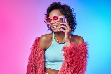Moda elbiseli mutlu Afrikalı kadın renkli arka planda cep telefonuyla konuşuyor.