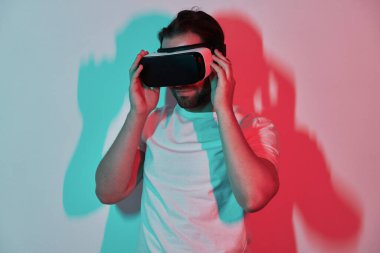 Kendine güvenen genç adam sanal gerçeklik gözlüklerini ayarlıyor. Arka planda renkli gölgeler var.