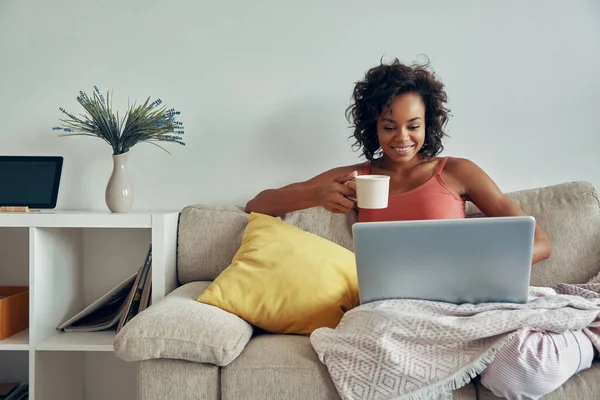 Schöne Afrikanerin Mit Laptop Und Kaffeetasse Während Sie Hause Auf — Stockfoto