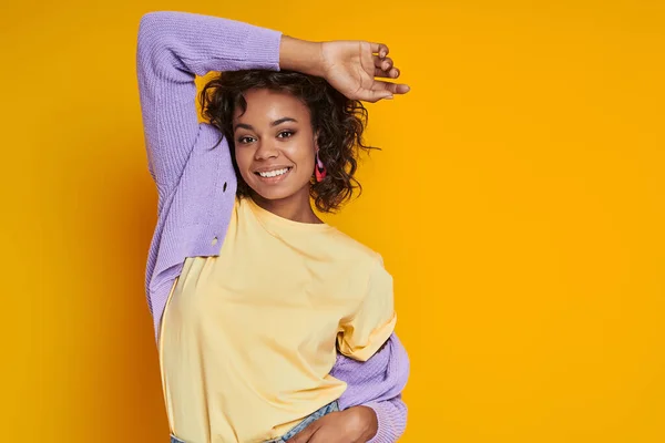 Happy African woman looking at camera and smiling while standing against yellow background