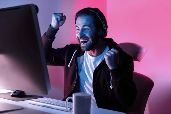 Happy young man looking at the computer monitor and gesturing against colorful background
