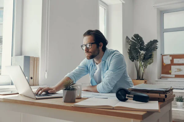 Joven Concentrado Usando Portátil Mientras Está Sentado Lugar Trabajo Oficina — Foto de Stock