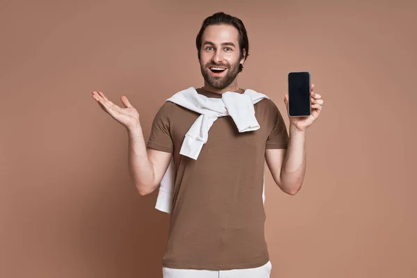Joven Feliz Sosteniendo Teléfono Inteligente Gesto Mientras Está Pie Sobre — Foto de Stock