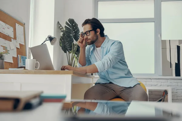 Selbstbewusster Junger Mann Sitzt Mit Laptop Seinem Arbeitsplatz Büro — Stockfoto