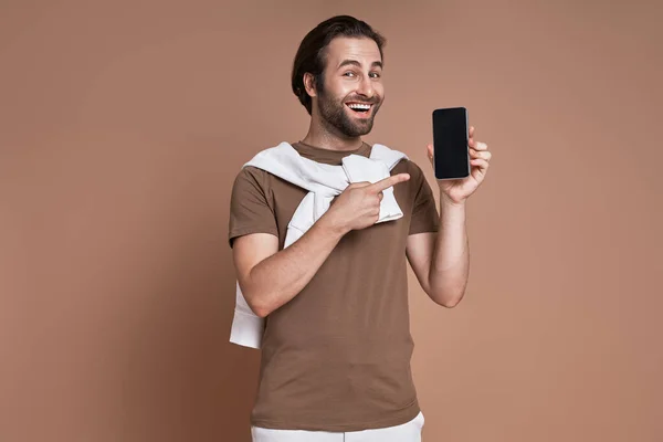 Feliz Joven Apuntando Teléfono Inteligente Mientras Está Pie Sobre Fondo — Foto de Stock