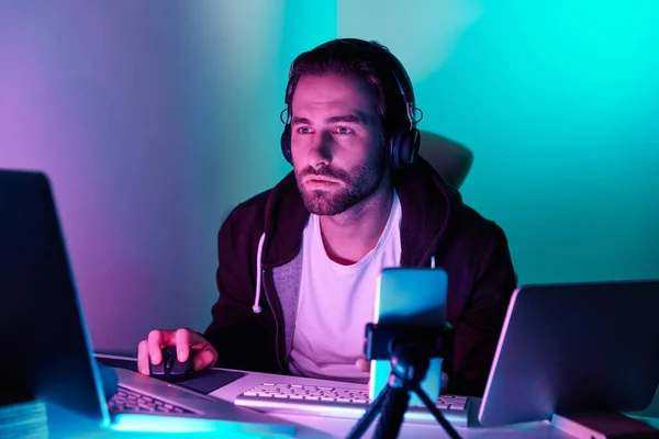 Concentrated young man looking at the computer monitor during live stream against colorful background
