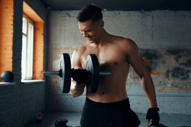 Kas yığını genç adam spor salonunda dambılla antrenman yaparken konsantre görünüyor.