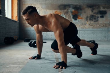 Kendine güvenen genç adam spor salonunda egzersiz yaparken konsantre görünüyor.