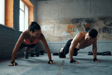 Spor salonunda şınav çekerken birbirlerine bakan genç ve zinde bir çift.