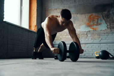 Formda genç bir adam spor salonunda halterle egzersiz yaparken konsantre olur.