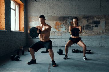 Konsantre genç adam ve kadın spor salonunda ağırlık çalışması yapıyorlar.