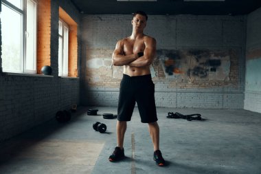 Spor salonunda kollarını kavuşturan yakışıklı, kaslı bir adam.