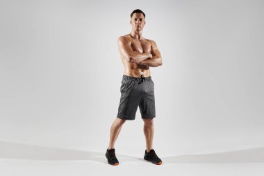 Yakışıklı kaslı adam beyaz arka planda dururken kollarını çapraz tutuyor.