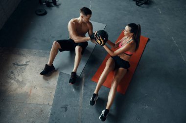Spor salonundaki spor minderlerinde otururken tıp topuyla egzersiz yapan genç çiftin en iyi görüntüsü.