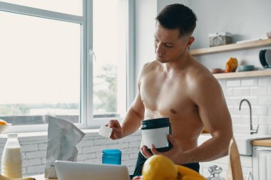 Kendine güvenen zinde bir adam mutfakta dururken protein içeceği hazırlıyor.