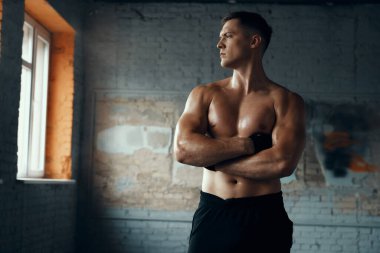 Yakışıklı kaslı adam spor salonunda kollarını çapraz tutuyor.