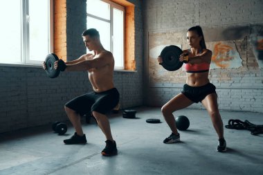 Spor salonunda ağırlık çalışırlarken konsantre olmuş gibi görünen genç bir çift.