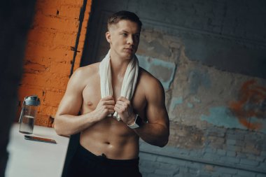 Spor yaparken omuzlarında havlu taşıyan kaslı bir adam.