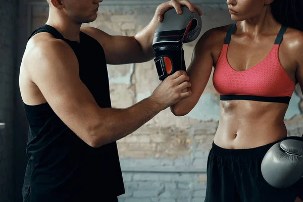 Close-up of male coach helping woman to wear boxing glove in gym