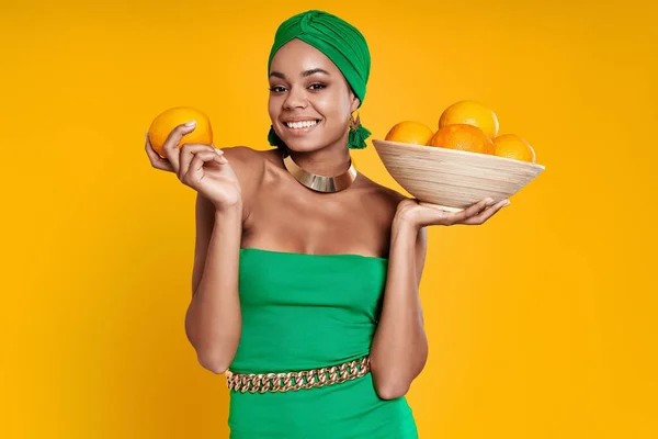 Счастливая Африканская Женщина Традиционных Головных Уборах Держит Апельсины Жёлтом Фоне — стоковое фото