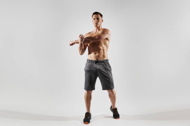 Mükemmel vücutlu genç adam beyaz arka plana karşı esneme egzersizleri yapıyor.