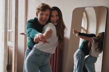 Evde birlikte eğlenirken el ele tutuşup gülümseyen neşeli genç çift.