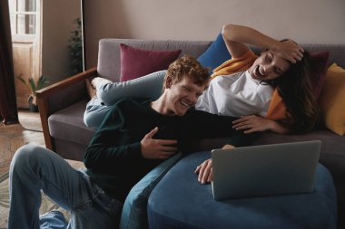 Güzel genç çift dizüstü bilgisayar kullanıyor ve evde dinlenirken gülüyorlar.