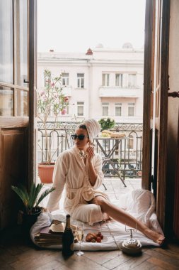 Bornozlu güzel bir kadın otelin balkonunda otururken telefon kullanıyor.