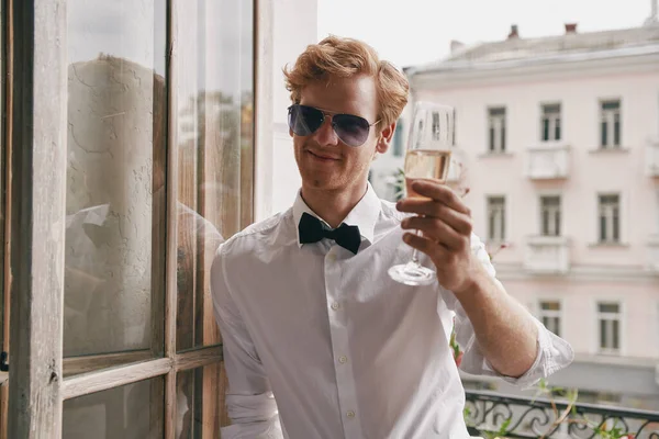 Vrolijke Jongeman Shirt Vlinderdas Toasten Met Champagne Terwijl Leunend Balkondeur — Stockfoto
