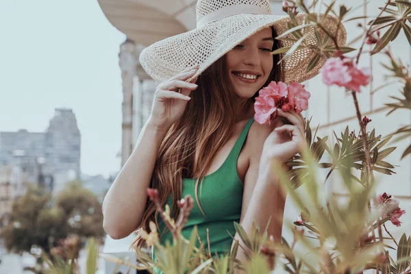 Ελκυστική Νεαρή Γυναίκα Προσαρμόζει Κομψό Καπέλο Της Και Μυρίζει Λουλούδια — Φωτογραφία Αρχείου
