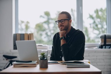 Ofisinde çalışırken dizüstü bilgisayara bakan düşünceli bir genç.