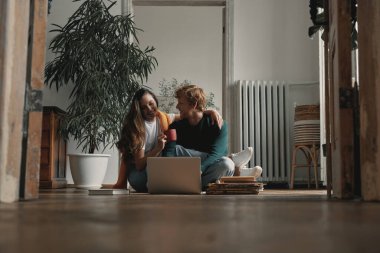 Evde birlikte otururken dizüstü bilgisayar kullanan mutlu genç çift.