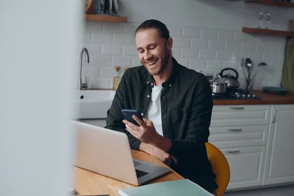 Joven Alegre Usando Teléfono Inteligente Mientras Trabaja Desde Cocina Doméstica — Foto de Stock