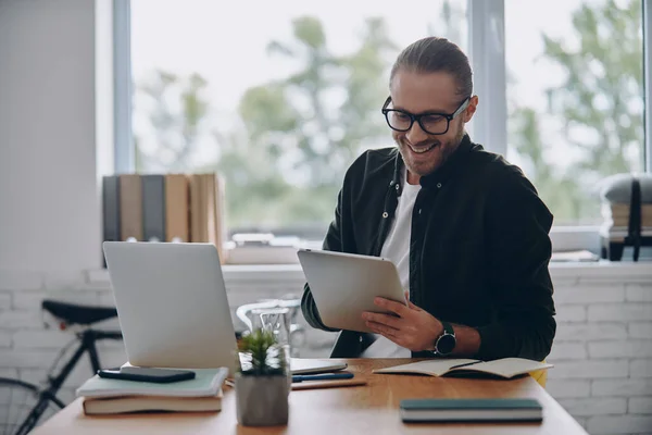 Χαρούμενος Νεαρός Που Χρησιμοποιεί Ψηφιακή Ταμπλέτα Ενώ Κάθεται Στο Γραφείο — Φωτογραφία Αρχείου