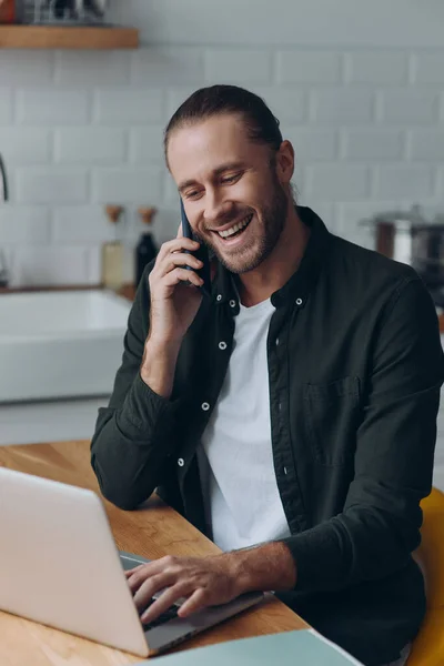 Joven Alegre Hablando Teléfono Móvil Uso Computadora Portátil Mientras Está — Foto de Stock