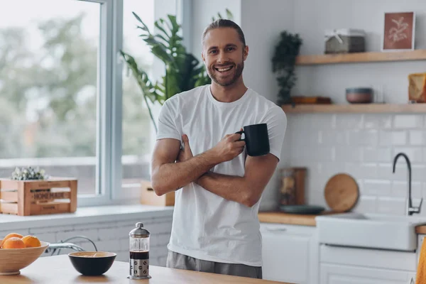 Joven Guapo Disfrutando Del Café Sonriendo Mientras Está Pie Cocina —  Fotos de Stock