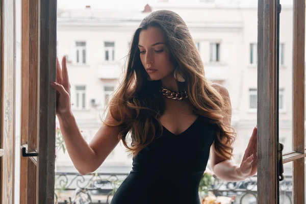 Beautiful young woman in cocktail dress opening the balcony doors